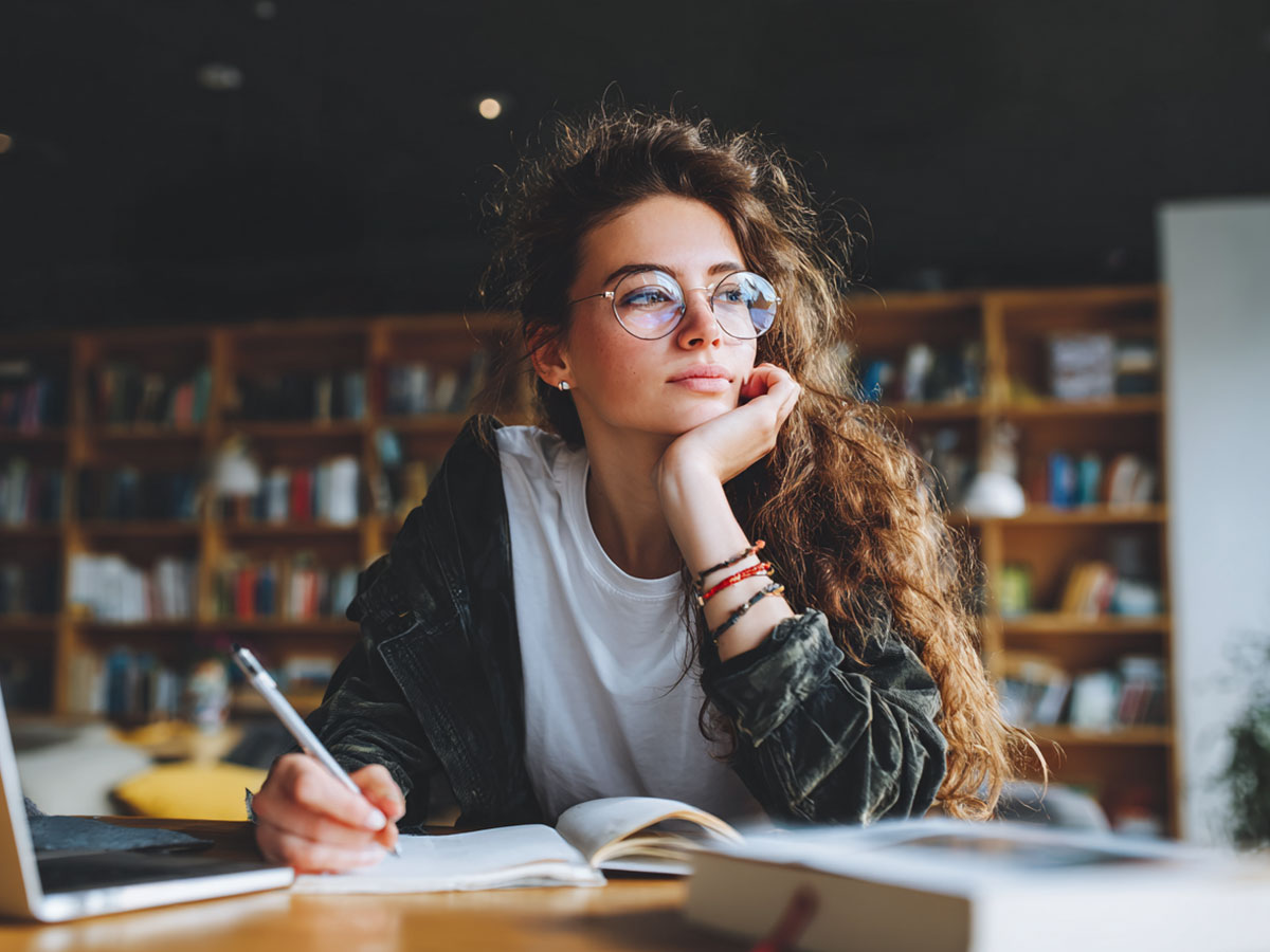 Eine Frau mit langen, lockigen Haaren schreibt ein Buch.